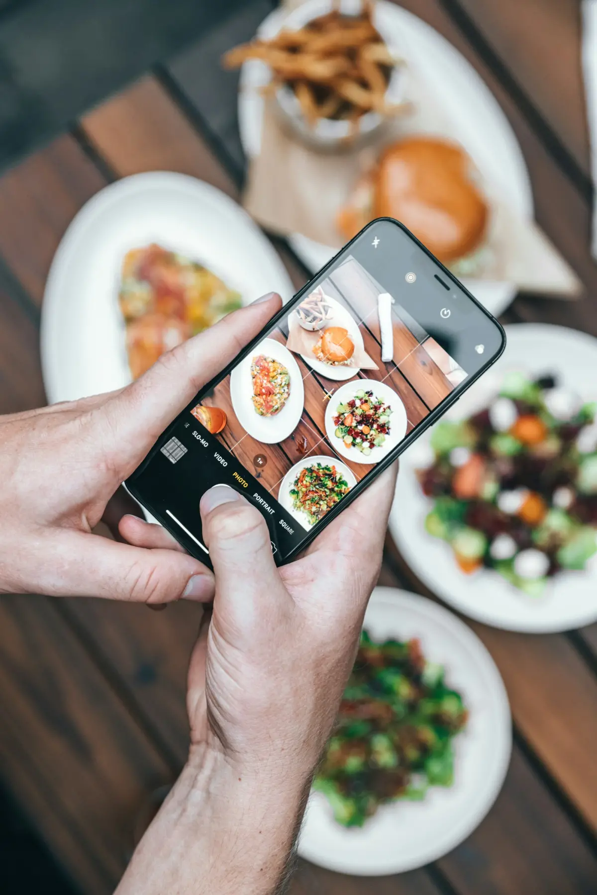 Hands holding a phone to photograph several dishes on a table