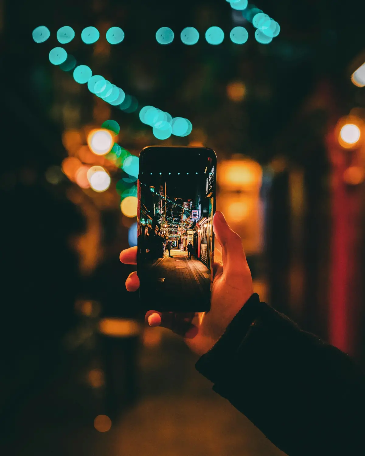 Person photographing a night street with colourful lights on a smartphone